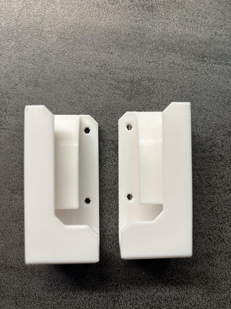 Pu&ograve; includere: Due supporti a parete bianchi e rettangolari con un design a forma di U. Ogni supporto ha un foro per l'hardware di montaggio. I supporti sono realizzati in un materiale liscio e solido e sono progettati per contenere un oggetto.
