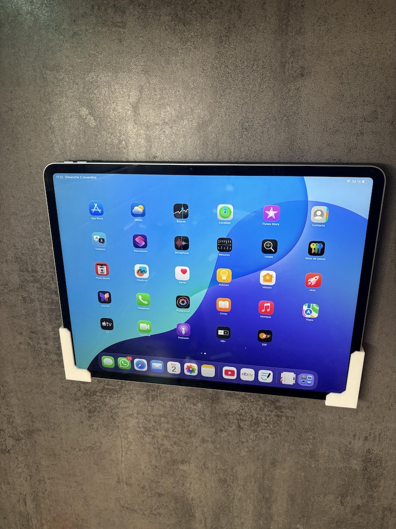 Pu&ograve; includere: Un tablet con schermo blu e bianco che mostra icone di app, tenuto in posizione da staffe angolari bianche. Lo schermo mostra una variet&agrave; di icone di app colorate, tra cui app di social media e intrattenimento. Il tablet &egrave; montato su un muro grigio.