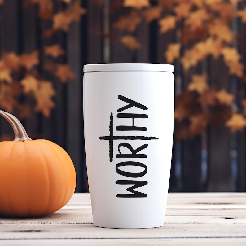 Peut inclure: Un mug de voyage blanc avec le mot "WORTHY" en lettres noires verticales. Le mug est cylindrique avec un couvercle blanc. Une citrouille orange est &agrave; gauche du mug sur une surface en bois, avec des feuilles d'automne en arri&egrave;re-plan.