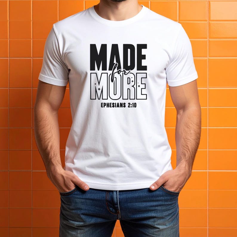 Peut inclure: T-shirt blanc avec l'inscription "MADE for MORE" en noir, avec "Ephesians 2:10" en dessous. Le t-shirt est &agrave; manches courtes. La personne qui porte le t-shirt a les mains dans les poches. Le fond est un mur carrel&eacute; orange.