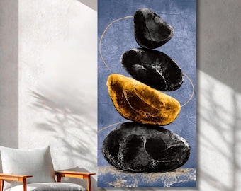 Könnte beinhalten: Ein vertikaler Wandkunstdruck mit einem Stapel aus vier glatten Steinen vor einem strukturierten blauen Hintergrund. Der oberste, der zweite und der unterste Stein sind schwarz, während der dritte Stein goldfarben ist. Dünne, geschwungene goldene Linien verlaufen um die Steine.