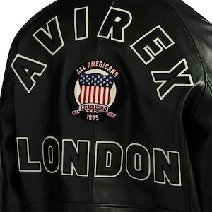 May include: Black leather jacket with white embroidered lettering spelling "AVIREX" and "LONDON". A circular patch features the American flag and the words "ALL AMERICANS ESTABLISHED 1975 N.Y."