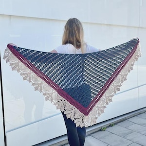 Könnte beinhalten: Handgefertigter Schal in Dreiecksform. Der Schal hat eine dunkelblaue Mitte, einen bordeauxfarbenen Rand und eine beige Spitzenkante. Der Schal wird offen gehalten, um sein kompliziertes Häkeldesign und seine Farbpalette zu zeigen.