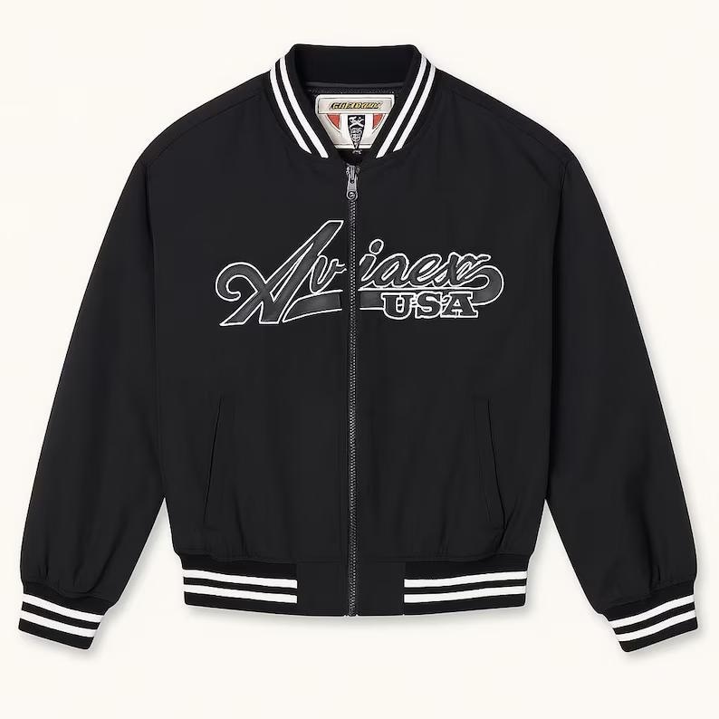 May include: Black bomber jacket with white and black striped trim on the collar, cuffs, and hem. The jacket features a full-length zipper and the word "Aviaex USA" in white script across the chest.