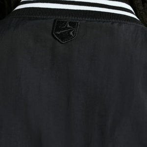 May include: Black bomber jacket with a white and black striped collar. The jacket features a small, black emblem on the upper back. The jacket is made of a smooth, possibly nylon, material.