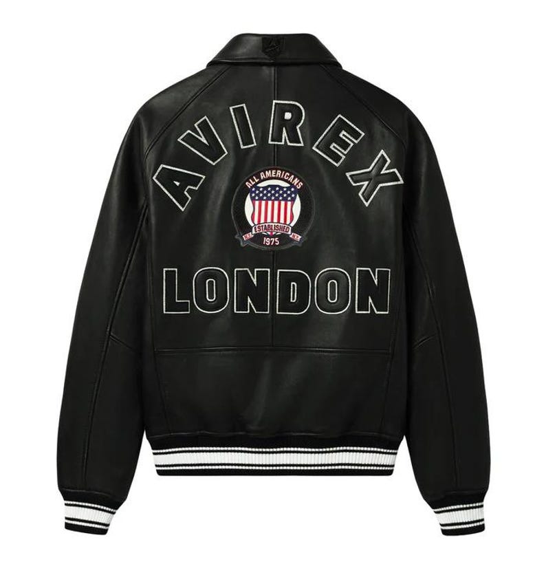 May include: Black leather jacket with white lettering spelling "AVIREX" and "LONDON". A circular patch features the American flag and the words "ALL AMERICANS ESTABLISHED 1975". The jacket has a white and black striped trim.