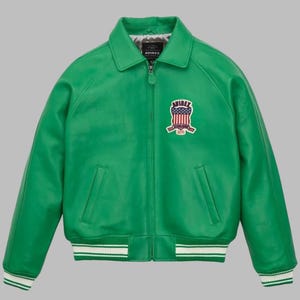 May include: A vibrant green leather jacket with a classic bomber style. Features a collared neckline, a zip-up front, and two front pockets. The jacket has a white and green striped ribbed hem and cuffs. An embroidered patch with a shield design and the brand name is on the chest.