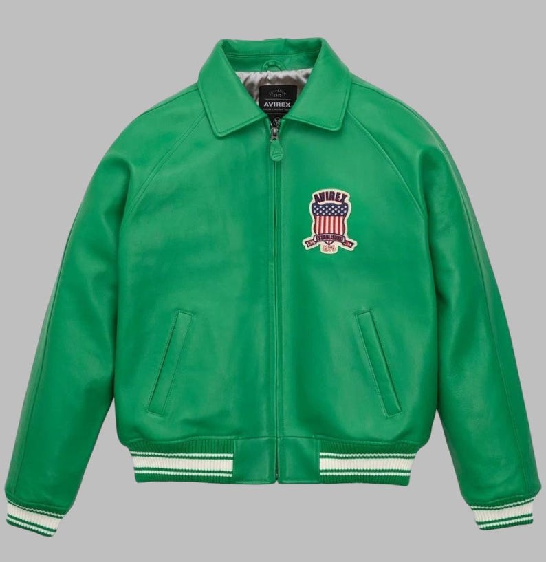 May include: A vibrant green leather jacket with a classic bomber style. Features a collared neckline, a zip-up front, and two front pockets. The jacket has a white and green striped ribbed hem and cuffs. An embroidered patch with a shield design and the brand name is on the chest.