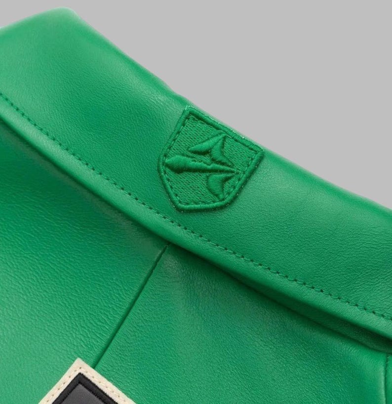 May include: Close-up of a bright green leather item with a stitched seam. A green embroidered emblem, possibly a logo, is sewn onto the item. The emblem is a shield shape with a stylized design.