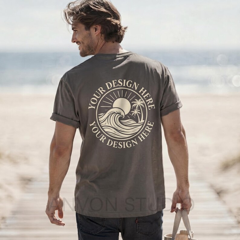 May include: A gray t-shirt with a circular design on the back featuring a sun, waves, and palm trees. The text "YOUR DESIGN HERE" is printed around the design. The shirt has rolled-up sleeves.