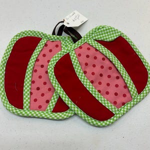 May include: Two handmade, quilted pot holders. Each pot holder features a red and pink design with a green and white gingham border. The pink sections have red polka dots. A tag reads "For House" and a price.