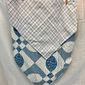 May include: A two-layer fabric item, possibly a bandana or scarf, hanging from a pink hanger. The top layer features a white and navy blue plaid pattern. The bottom layer has a teal and white floral and geometric design.