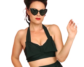 May include: A woman wearing a black halter top swimsuit with a bow detail. She is wearing heart-shaped sunglasses and has her hair styled in a vintage updo.
