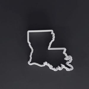 Könnte beinhalten: Ein weißer Kunststoff-Ausstecher in Form des Umrisses des US-Bundesstaates Louisiana. Der Ausstecher verfügt über einen durchgehenden, erhöhten Rand, der die markanten geografischen Grenzen des Staates nachbildet, einschließlich der gezackten Küstenlinie.