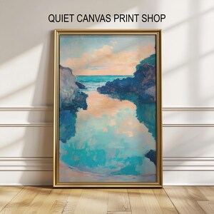 Op de afbeelding: Een ingelijst landschapsschilderij met een gouden lijst. Het kunstwerk toont een kustlandschap met turquoise water, rotsachtige kliffen en een perzikkleurige lucht. De tekst "QUIET CANVAS PRINT SHOP" staat bovenaan.