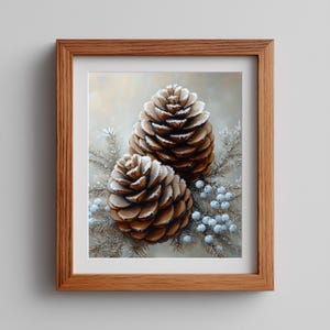 Könnte beinhalten: Gerahmter Druck mit zwei großen braunen Tannenzapfen, die mit weißem Frost bedeckt sind. Sie liegen auf gefrorenen Tannenzweigen und kleinen blauen Beeren. Das Kunstwerk befindet sich in einem Holzrahmen.
