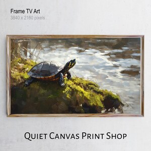 Op de afbeelding: Een ingelijste digitale kunstprint met een schildpad op een met mos begroeide oever naast water. De schildpad heeft een donker schild met gele markeringen. Het kunstwerk is ingelijst in een lichtbruine houten lijst. De tekst "Frame TV Art" en "QUIET CANVAS PRINT SHOP" zijn zichtbaar.