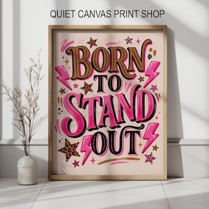 以下が含まれることがあります： 「BORN TO STAND OUT」の文字が大胆なピンクと茶色のフォントで描かれた、額入りのアートプリント。稲妻、星、ヒョウ柄のアクセントが特徴です。「QUIET CANVAS PRINT SHOP」の文字が上部にあります。