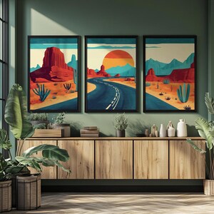 May include: Three framed art prints depicting a desert landscape with a road, mountains, and cacti. The artwork features a color palette of red, blue, orange, and beige. The prints are displayed above a wooden cabinet with plants.