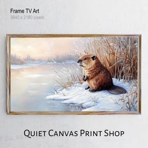 Op de afbeelding: Een ingelijste print van een bever in een winterlandschap. Het kunstwerk toont een bruine bever die op een besneeuwde oever bij een watermassa zit. De achtergrond toont een zachte, kleurrijke zonsondergang. De lijst is van hout.