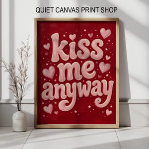 Puede incluir: Una impresión artística enmarcada con el texto "Kiss me anyway" en letras rosas sobre un fondo rojo. La impresión presenta corazones y estrellas rosas. El texto "Quiet Canvas Print Shop" está en la parte superior.