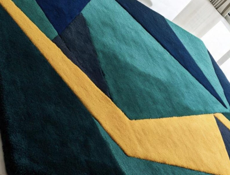 May include: Geometric patterned rug featuring a combination of teal, navy, and yellow. The design incorporates angular shapes and a textured surface, creating a modern and artistic aesthetic. The rug's color palette adds a vibrant touch to any room.