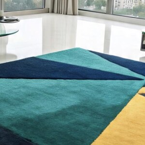 May include: A geometric area rug with a modern design. The rug features a teal, navy blue, and yellow color scheme. The rug's design includes triangular and rectangular shapes, creating a contemporary look. The rug is placed on a white floor.
