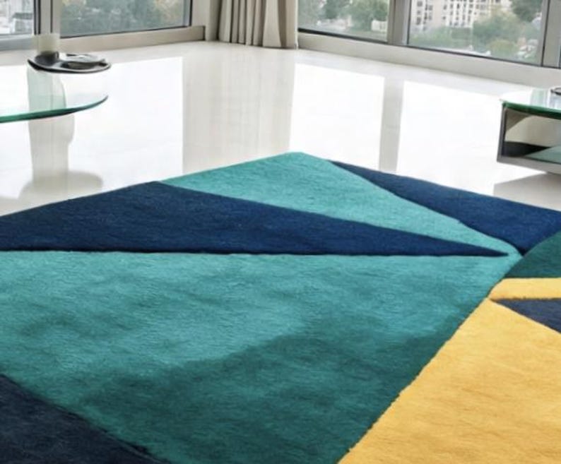 May include: A geometric area rug with a modern design. The rug features a teal, navy blue, and yellow color scheme. The rug's design includes triangular and rectangular shapes, creating a contemporary look. The rug is placed on a white floor.