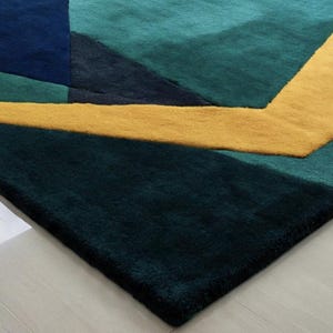 May include: A geometric area rug featuring a modern design with a combination of teal, navy, and gold colors. The rug's pattern includes angular shapes and lines, creating a contemporary aesthetic. The rug is made of a soft, plush material.
