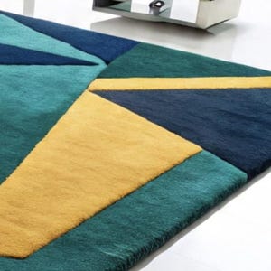 May include: A geometric area rug featuring a pattern of triangles and rectangles in shades of teal, navy blue, and yellow. The rug has a soft, plush texture and is designed for indoor use. The rug's dimensions are not visible in the image.