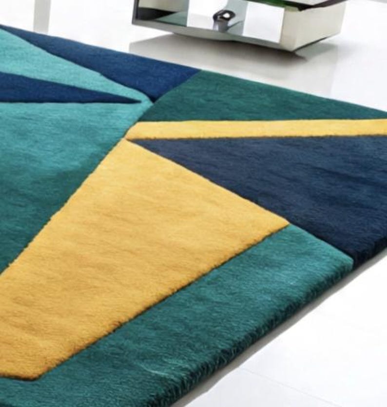 May include: A geometric area rug featuring a pattern of triangles and rectangles in shades of teal, navy blue, and yellow. The rug has a soft, plush texture and is designed for indoor use. The rug's dimensions are not visible in the image.