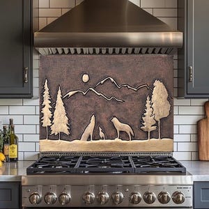 Puede incluir: Un protector contra salpicaduras de cocina de color cobre con un diseño en relieve de lobos aullando a la luna, sobre un fondo de montañas y bosque. El diseño está enmarcado por detalles dorados y está montado sobre una estufa de gas.