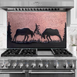 May include: A decorative kitchen backsplash featuring a copper-colored background with a textured pattern. Two black silhouettes of moose are engaged in a head-to-head confrontation, set against a backdrop of stylized trees and grass.