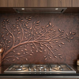 May include: A copper-coloured kitchen backsplash featuring a raised relief design of a tree branch with leaves. The backsplash is above a stainless steel gas hob. A copper utensil holder with utensils is on the counter.