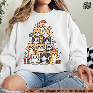 May include: White sweatshirt featuring a Christmas tree design made of cartoon cats. The cats are in various colors, wearing Santa hats and holding ornaments. The text "PNG File - Digital Download Only (No Physical Item)" is at the bottom.