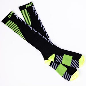 May include: Black athletic socks with neon green and white details. The socks display the word "LIMIT" at the top, with a striped design and text. The heels and toes are bright yellow.