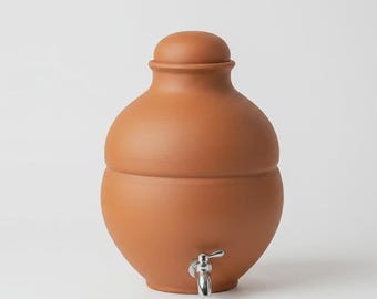 May include: A terracotta water dispenser with a rounded body and a matching lid. The vessel features a smooth, matte finish in a warm reddish-brown clay tone. A polished silver-colored metal spigot is attached to the lower front section.