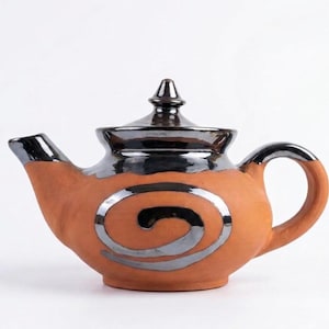 May include: A terracotta teapot featuring a metallic silver glaze on the lid, spout, handle, and a prominent spiral design on the body. The teapot has a rounded shape with a pointed lid finial and a smooth, matte finish on the clay surface.