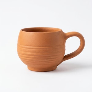 Peut inclure: Une tasse de couleur terre cuite avec un corps arrondi et une anse incurvée. La tasse présente des rainures horizontales sur sa circonférence. La tasse est en céramique et convient aux boissons chaudes ou froides.
