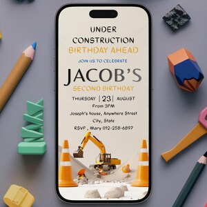 Puede incluir: Un smartphone muestra una invitación de cumpleaños con un tema de construcción. La invitación dice "Under Construction Birthday Ahead" y "Jacob's Second Birthday". La imagen está rodeada de herramientas de construcción y lápices de juguete.