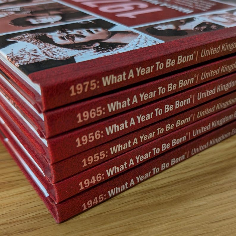 K&ouml;nnte beinhalten: Ein Stapel aus sechs roten Hardcover-B&uuml;chern mit wei&szlig;em Text auf den Buchr&uuml;cken. Jeder Buchr&uuml;cken zeigt das Jahr gefolgt vom Titel What A Year To Be Born | United Kingdom. Die aufgef&uuml;hrten Jahre sind 1975, 1965, 1956, 1955, 1946 und 1945.
