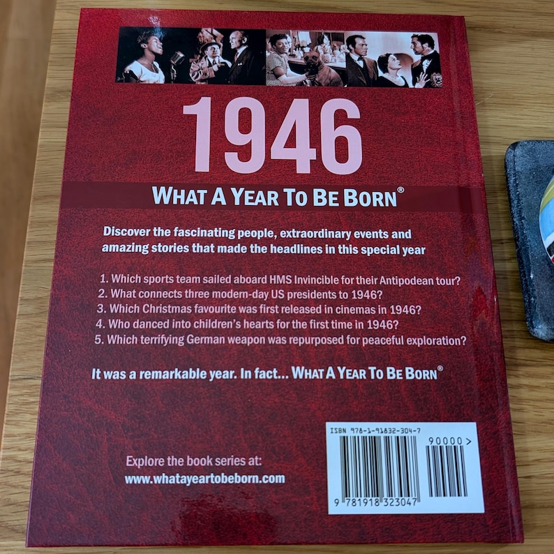 K&ouml;nnte beinhalten: Ein rotes gebundenes Buch mit dem Titel 1946 What A Year To Be Born. Die R&uuml;ckseite zeigt eine Collage aus historischen Schwarz-Wei&szlig;-Fotos, eine Liste mit f&uuml;nf Quizfragen, einen kurzen Text und einen Barcode mit ISBN 978-1-91832-304-7.