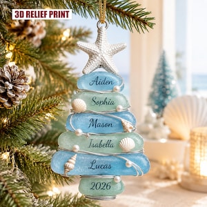 Puede incluir: Un adorno para árbol de Navidad con forma de pirámide, hecho de piezas de vidrio azul claro y verde espuma de mar apiladas y envueltas en alambre plateado. Incluye una estrella de mar blanca en la punta, pequeñas conchas blancas y los nombres Aiden, Sophia, Mason, Isabella, Lucas y 2026.