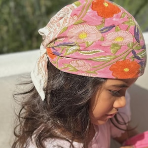 Peut inclure: Un foulard fleuri rose avec des fleurs orange et roses, des feuilles vertes et des accents violets. Le couvre-chef est noué dans le dos et est fait d'un tissu doux. Un accessoire élégant.