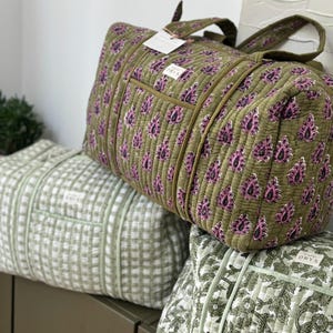 May include: Three quilted travel bags in shades of green. The top bag is olive green with a pink paisley pattern. The middle bag is light green with a grid pattern. The bottom bag is light green with a floral pattern. Each bag has a tag that says "ORYS".