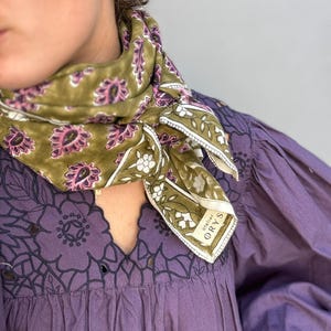 Può includere: Sciarpa paisley verde oliva e rosa con bordo floreale bianco. La sciarpa è drappeggiata su un vestito viola con dettagli floreali ritagliati. La sciarpa ha il testo "atelier ORYS" nell'angolo.