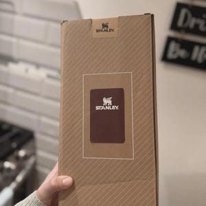 May include: A Stanley brand cardboard box with a brown and white logo. The box is a light brown color with diagonal lines. The Stanley logo is on the top and center of the box.