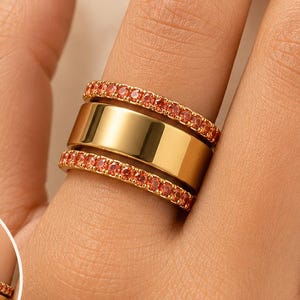 Puede incluir: Un realzador de anillo en tono dorado con dos bandas de brillantes piedras de circonita cúbica naranja, diseñado para usarse con un anillo Oura Gen 3 & 4. El texto en la imagen dice Compatible with Oura Ring Gen 3 & 4, Before Oura Ring Alone y After With Ring Enhancer.