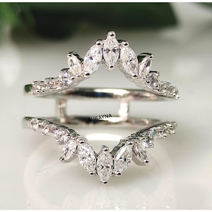 May include: A silver ring guard with marquise-cut and round-cut clear gemstones. The ring guard features a curved design with the word "AURAYNA" engraved on the band.