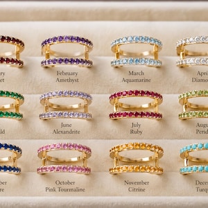 Puede incluir: Doce anillos dorados de doble banda, cada uno con una piedra preciosa de diferente color que representa las piedras de nacimiento de enero a diciembre, incluyendo granate, amatista, aguamarina, diamante, esmeralda, alejandrita, rubí, peridoto, zafiro, turmalina, citrino y turquesa.